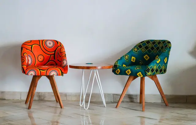 Two colorful chairs with a coffee table between them next to a white wall 